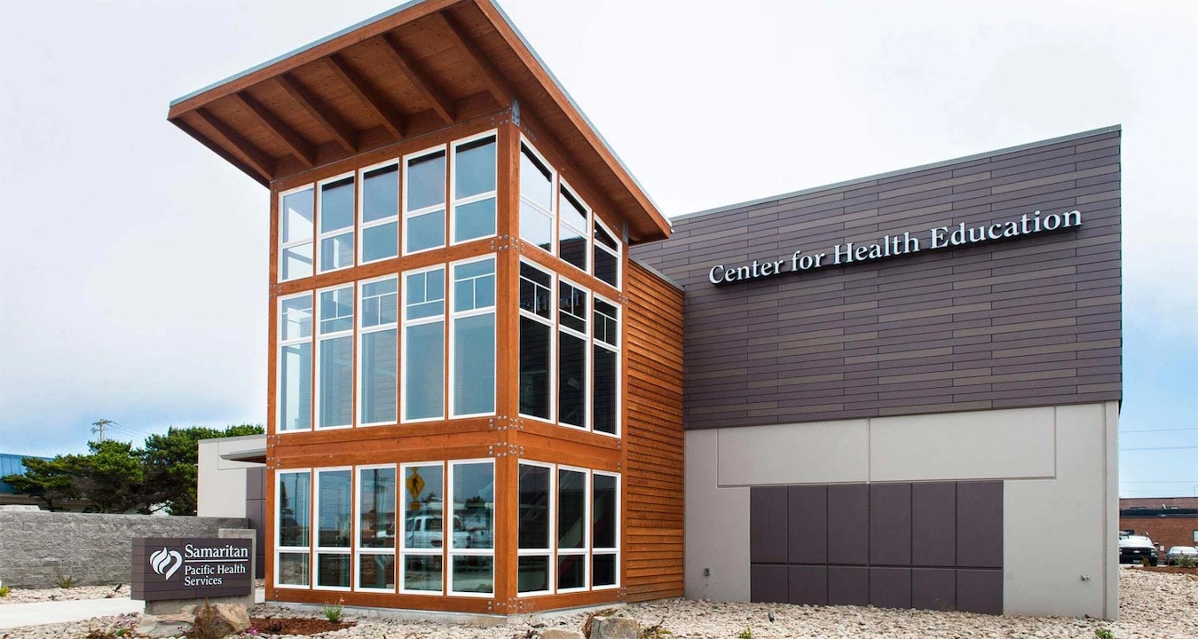 The Samaritan Center for Health Education in Newport, a two-story building with a tall wood-framed glass entrance, a sloped timber roof, and dark siding.